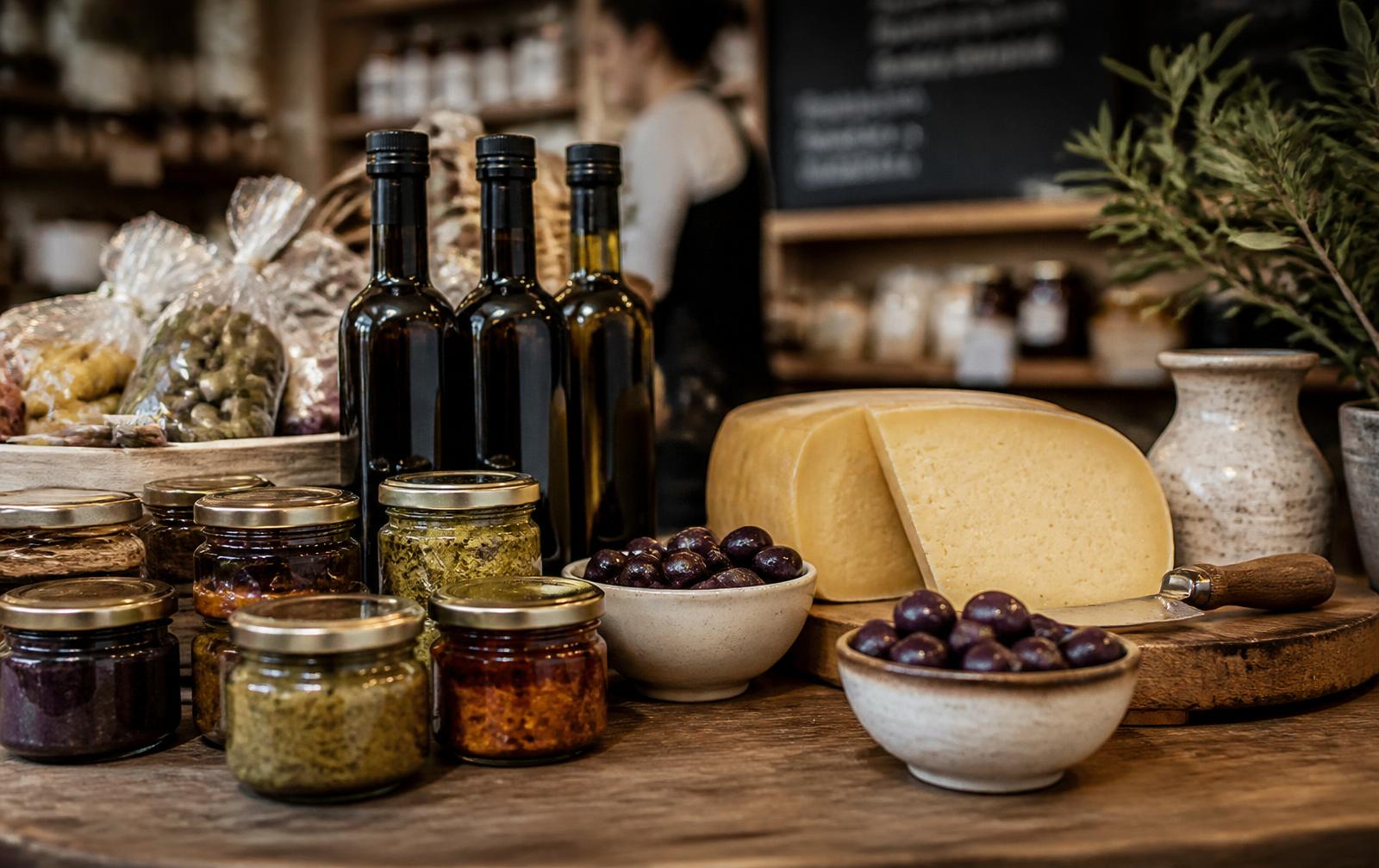 Premium Greek delicatessen counter with unbranded jars of spreads, olive oil bottles, Graviera cheese and bowls of Kalamata olives